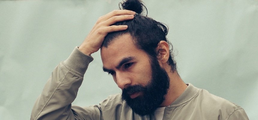 Guy with dark long hair and a beard holding his head with his hand