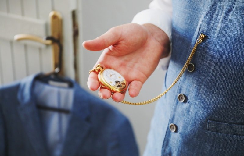 How to wear a Pocket Watch Man Holding Gold Pocket Watch in Hand While Wearing a Blue Suit