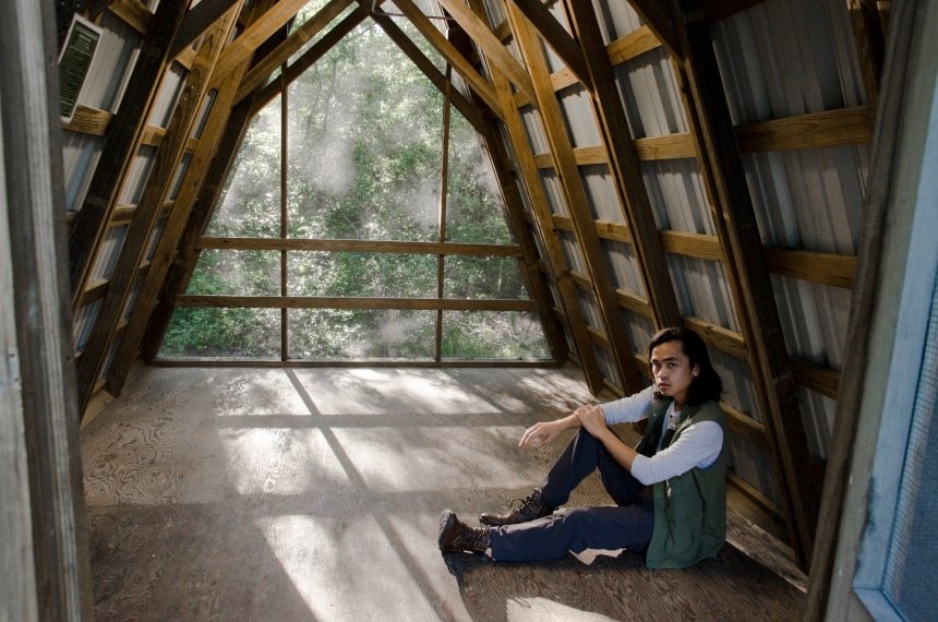 Male Model Wearing TravelSmith Voyager 15-Pocket Vest in Olive Inside of Cabin in Park And Looking at Camera