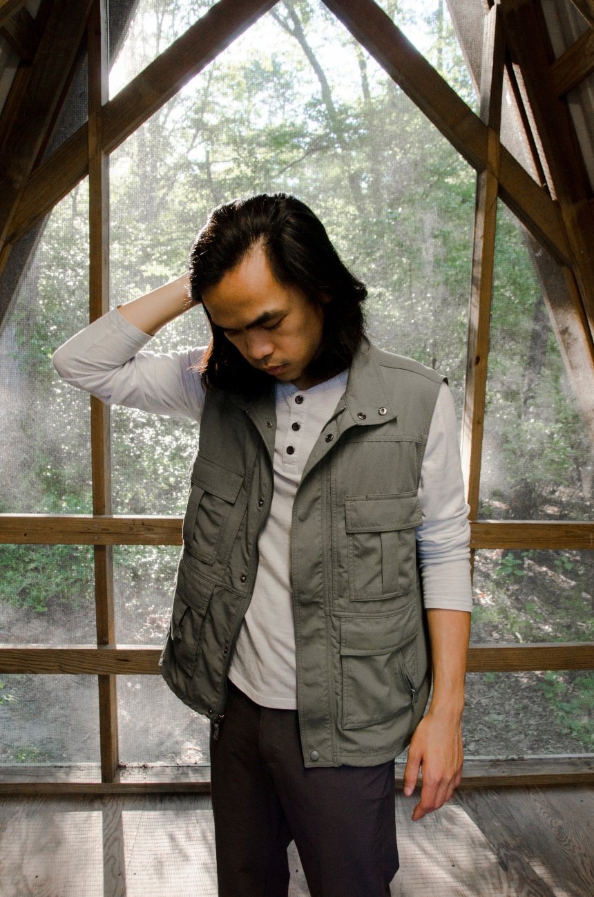 Male Model Wearing TravelSmith Voyager 15-Pocket Vest in Olive Inside of Cabin in Park And Looking Down