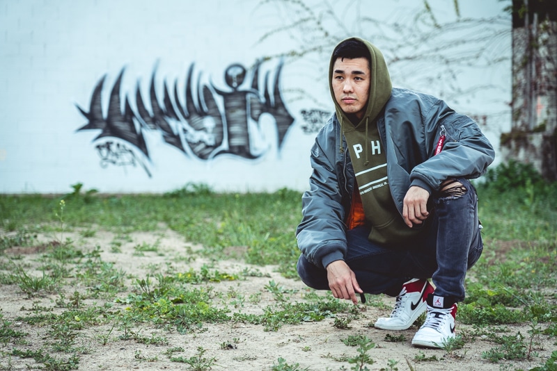 Man crouching in front of graffiti in bomber