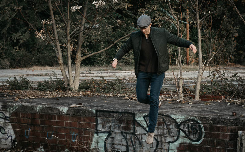 model jumping down from wall with jeans hat and bomber jacket