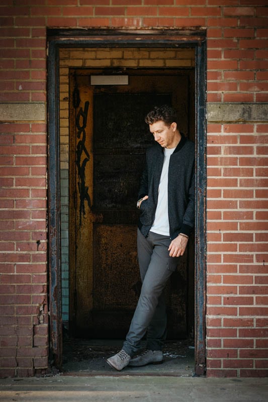 model leaning on brick doorway wearing paige jeans and bomber jacket