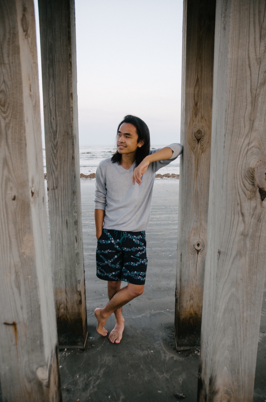 Model Wearing Stio CFS Board Short While Leaning Against a Pier And Smiling At The Beach