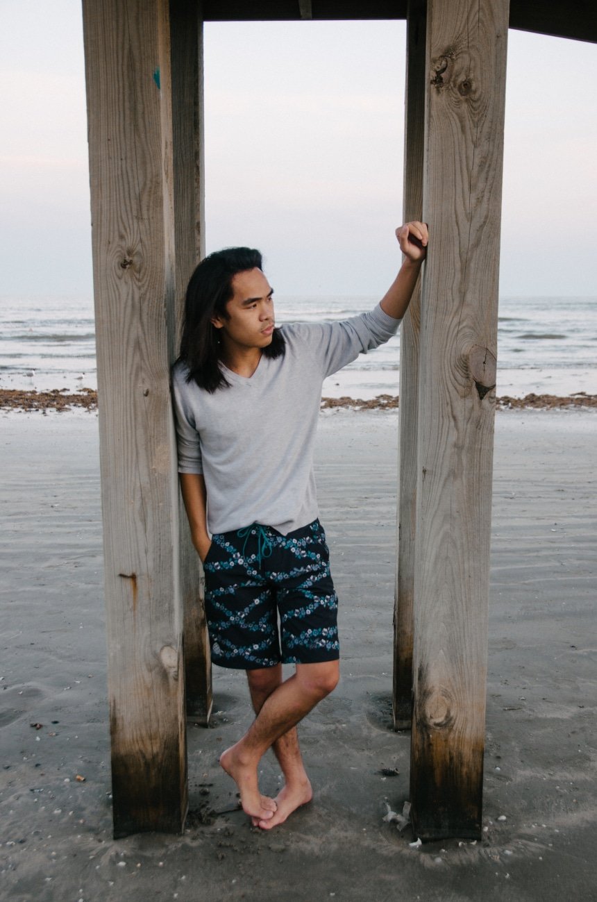 Model Wearing Stio CFS Board Short While Leaning Against a Pier At The Beach