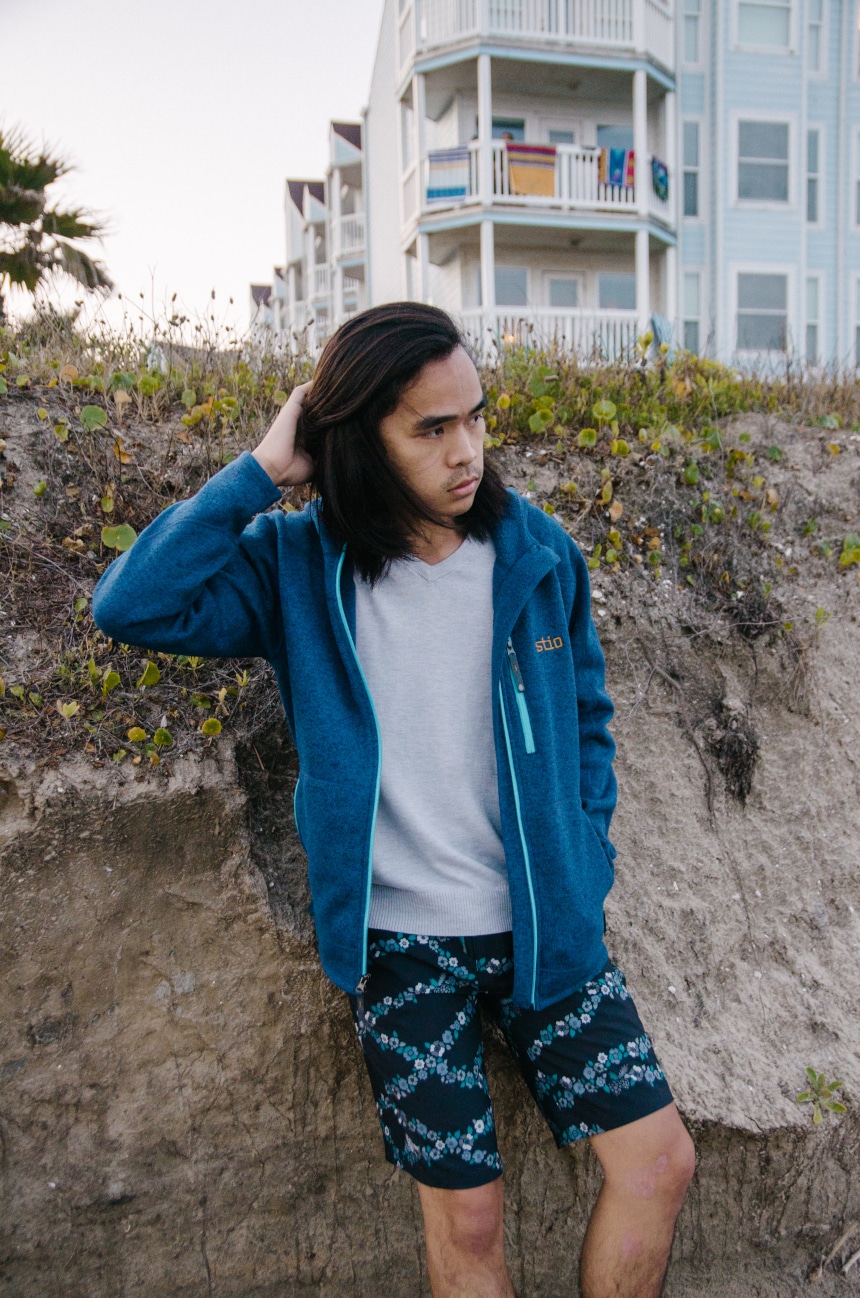 Model Wearing Stio Wilcox Fleece Hoodie and CFS Board Shorts Against Sand Dunes And Looking In The Distance