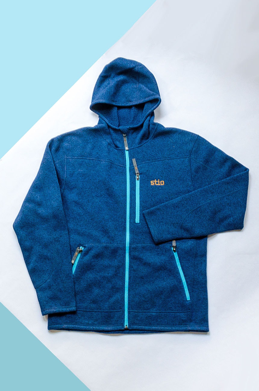 Stio Wilcox Fleece Hoodie in Larkspur Blue on Blue And White Paper Background