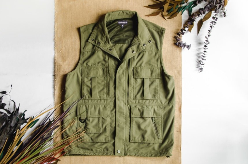 TravelSmith Voyager 15-Pocket Vest in Olive Sitting on Canvas Style Background with Leaves around