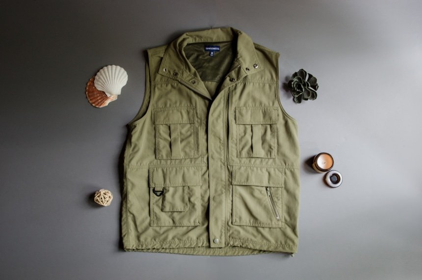 TravelSmith Voyager 15-Pocket Vest in Olive Sitting on Grey Background with Shells around